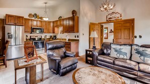 A modern kitchen with wooden cabinets, stainless steel appliances, and a leather recliner. - Black Canyon Inn Unit B4/5 (Estes Park)