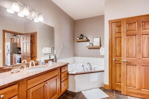 A modern bathroom with a double sink vanity, a freestanding bathtub, wooden doors, and a mirror with lights. - Black Canyon Inn Unit F1 Deluxe (Estes Park)