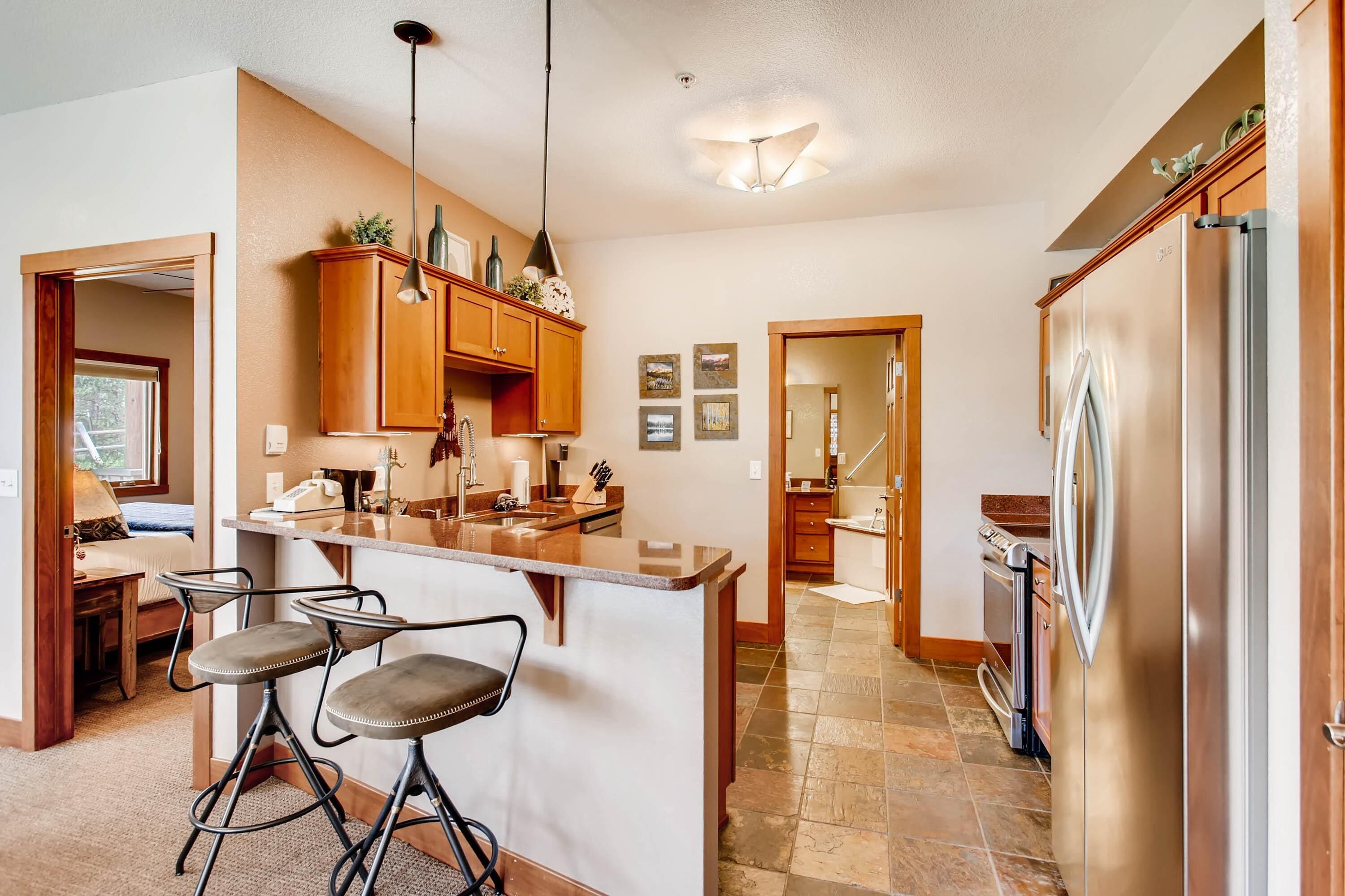A kitchen with a central island, bar stools, wooden cabinets, a stainless steel refrigerator, and a dining area with a table and chairs.