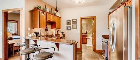 A kitchen with a central island, bar stools, wooden cabinets, a stainless steel refrigerator, and a dining area with a table and chairs.
