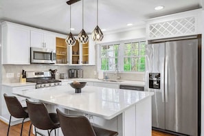 Una cocina moderna con armarios blancos, un refrigerador de acero inoxidable, horno empotrado y una isla grande con taburetes de bar.