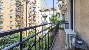 Ein Balkon mit Metallgeländer, einer Mülltonne und einem Gebäude mit mehreren Balkonen und Fenstern.