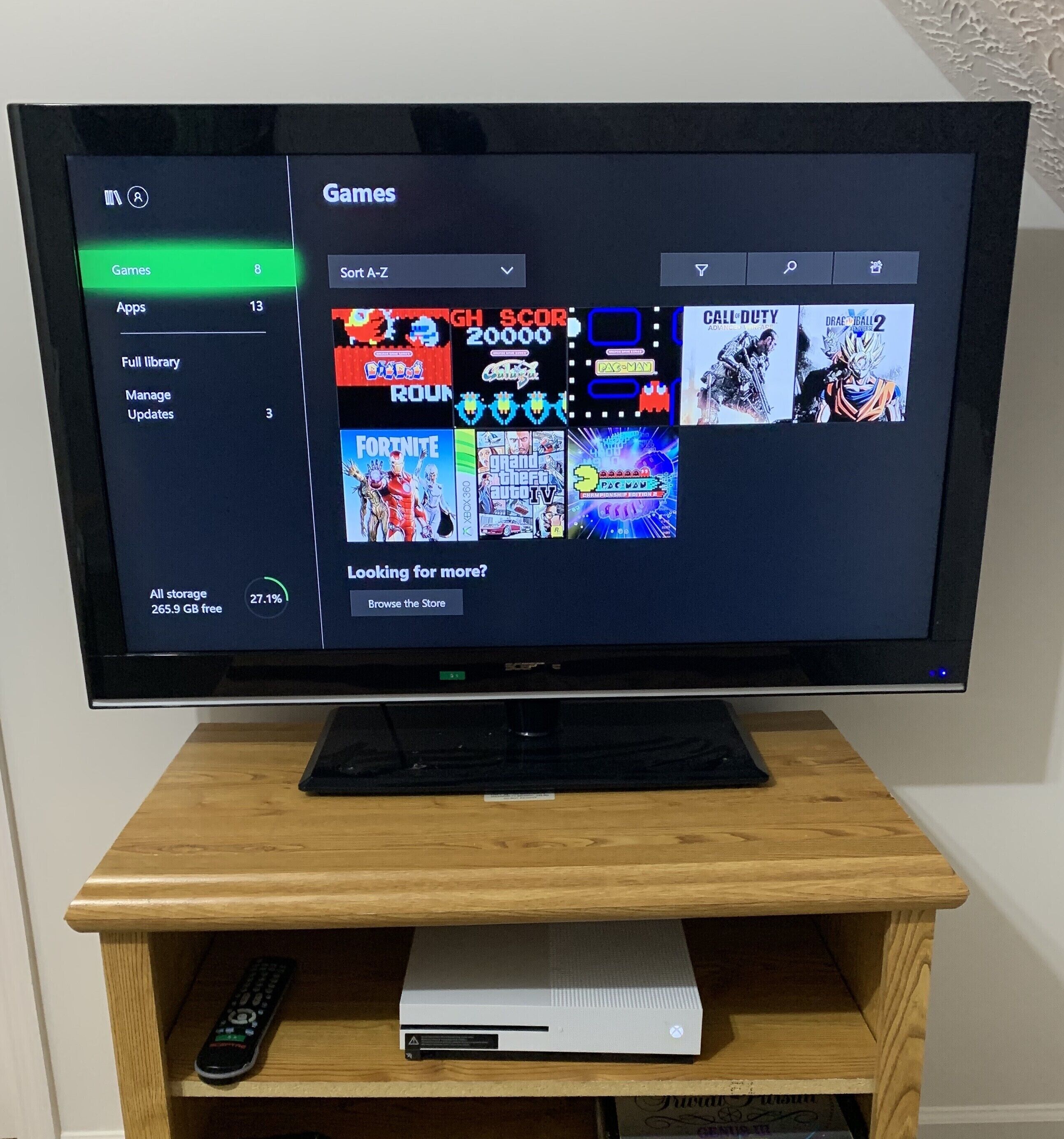 Een televisie op een houten standaard, toont een spelmenu met verschillende spelpictogrammen en een opslagindicator.