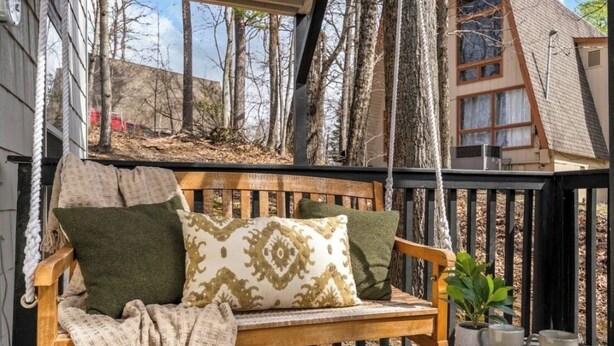 Eine hölzerne Bank mit Kissen, ein kleiner Tisch mit Keksen und ein Blumentopf auf einer Holzterrasse.
