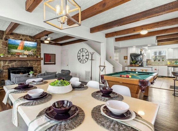 Un comedor con mesa de billar, chimenea y sala de estar con televisor.