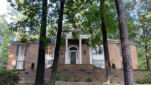 A two-story brick house with a front porch, a stone retaining wall, and a well-maintained lawn.