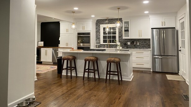 A modern kitchen with white cabinets, a stainless steel refrigerator, and a central island with stools.