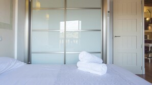 A bedroom with a large sliding glass door closet, a neatly made bed with white linens, and a visible bathroom with a shower and sink. - San Cipriano. Apartment with garage included (Toledo)
