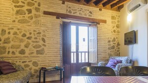 A room with stone walls, a wooden ceiling, a bed, a sofa, a TV, and a table with books. - San Cipriano. Apartment with garage included (Toledo)
