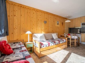 A cozy room with a wooden wall, a bed, a small table, and a kitchenette.