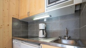 Une cuisine compacte dotée d’armoires en bois, d’un four à micro-ondes encastré, d’une machine à café et d’un lave-vaisselle.