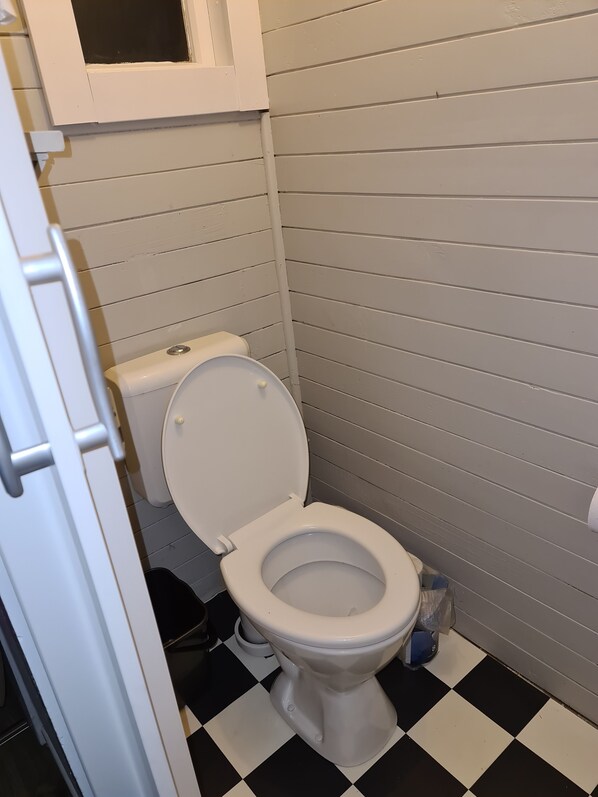 A small, white-framed bathroom with a toilet, a white door, and a black and white checkered floor. - Cute rustic bach, A home away from home. Located in beautiful mangakino (Waikato)