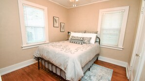 A bedroom with a bed, two windows with blinds, a ceiling fan, and a small rug.