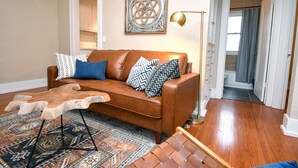 A living room with a brown leather sofa, patterned cushions, a wooden coffee table, and a decorative wall piece.