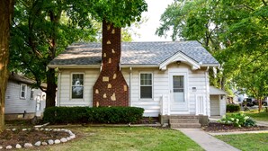 A single-story house with a brick chimney, white siding, and a front porch.