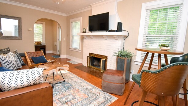 A living room with a fireplace, a television on a mantel, a sofa with patterned cushions, and a wooden chair.