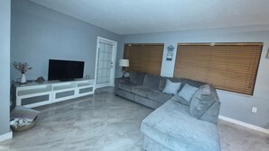A living room with a grey sofa, a television on a white entertainment unit, and a door with frosted glass panels. - Amazing house, 2 blocks from the beach (#1 in USA), close to the village.  (Siesta Key)