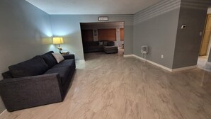 A living room with a dark-colored sofa, a lamp, and a small table. There is a sign on the wall that reads "Bench/High." The room has a tiled floor and a door leading to another room. - Amazing house, 2 blocks from the beach (#1 in USA), close to the village.  (Siesta Key)