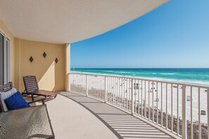 Varanda com vista para a praia, uma cadeira, uma mesa e um corrimão.