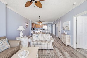 A living room with a sofa, a coffee table, a lamp, and a dining area with a chandelier.