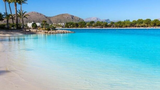 Una spiaggia con acqua cristallina, palme e montagne sullo sfondo.