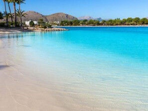 Una playa con aguas azul turquesa, palmeras y montañas al fondo.