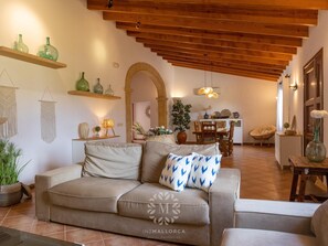 Una sala acogedora con sofá, vigas de madera, zona de comedor y una escalera.