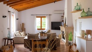 Un ampio soggiorno con soffitto in legno, camino, televisione e zona pranzo con tavolo e sedie.