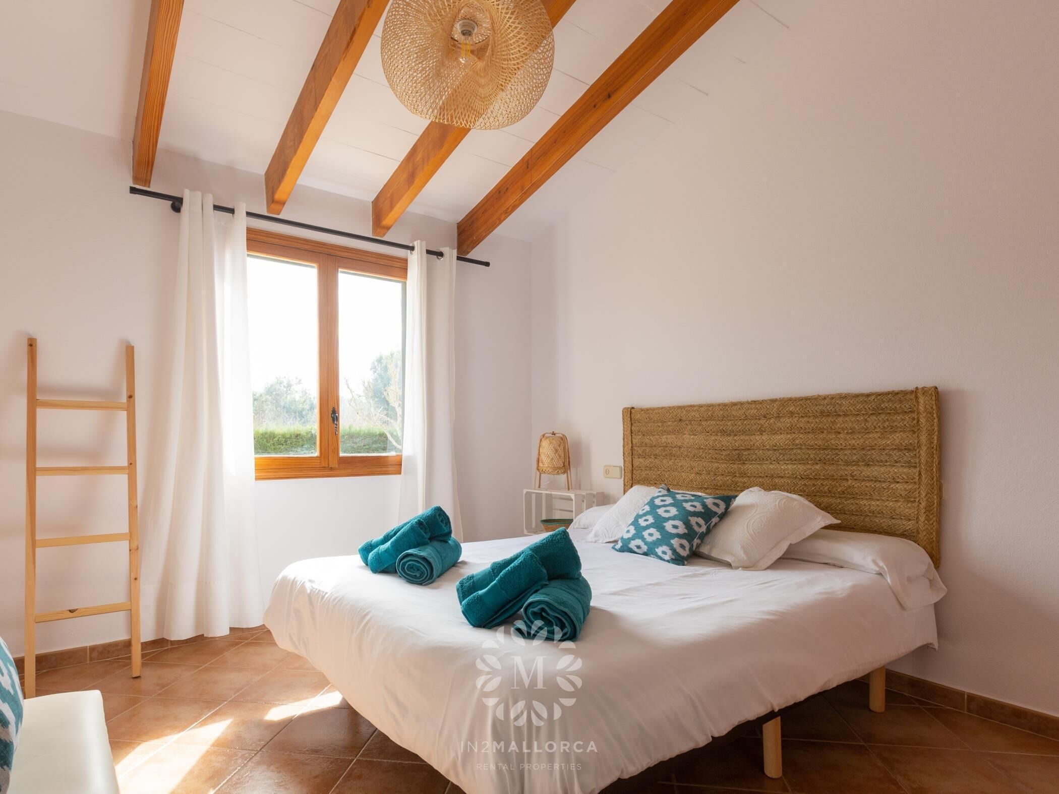 A bedroom with a bed, a window, a ladder, and a woven headboard.