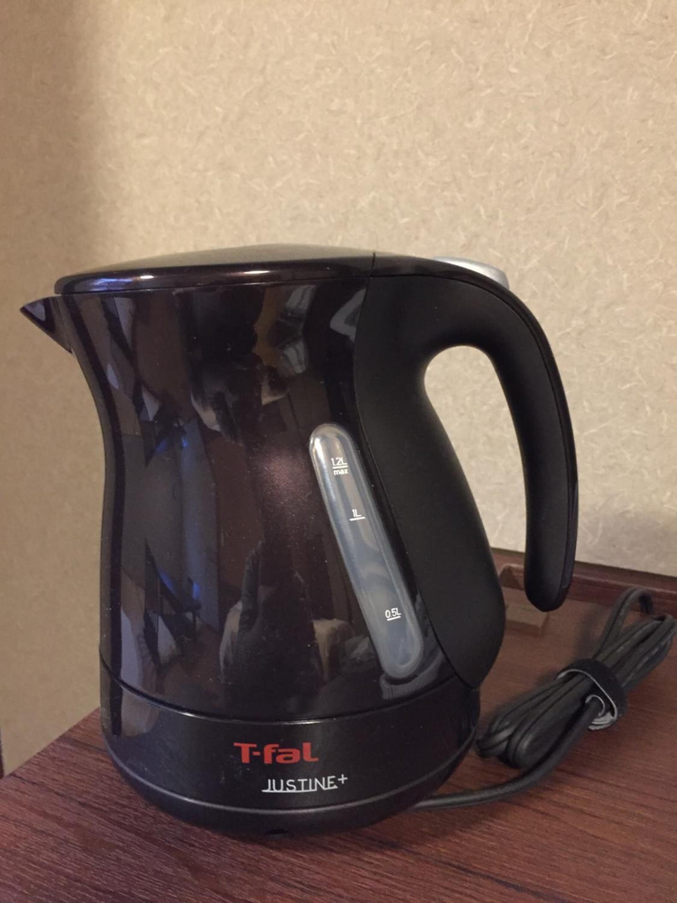 A black T-fal Justine+ electric kettle with a handle and a power cord.