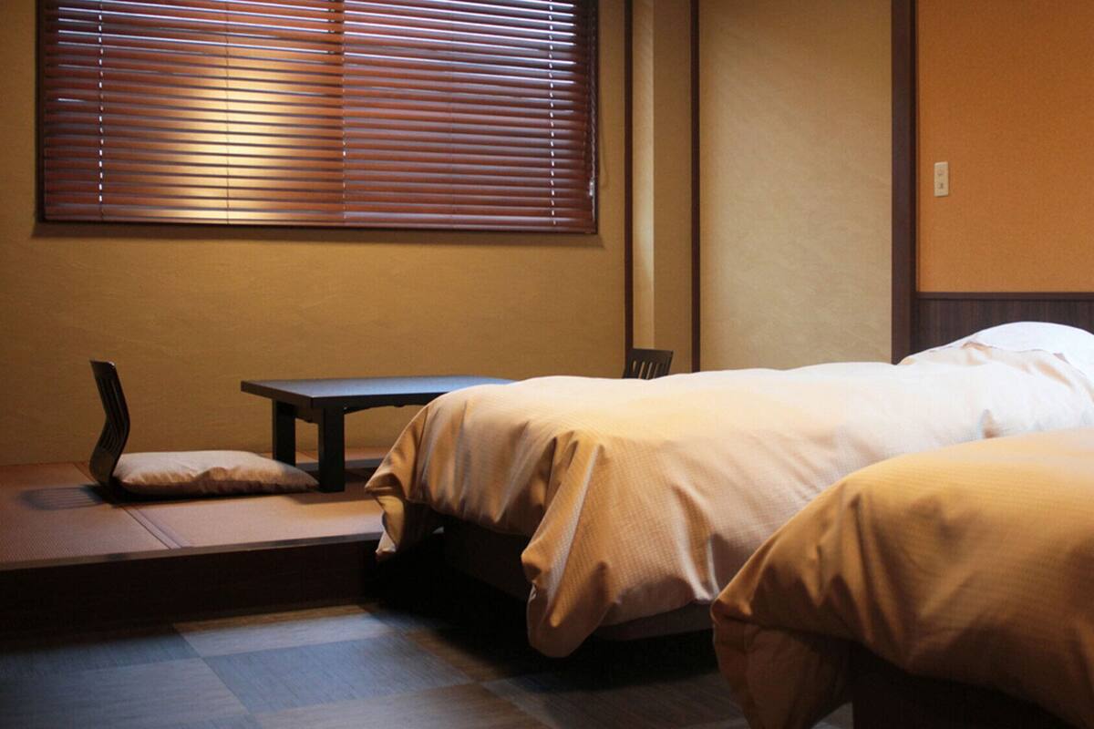A hotel room with two beds, a small table, and a bench.