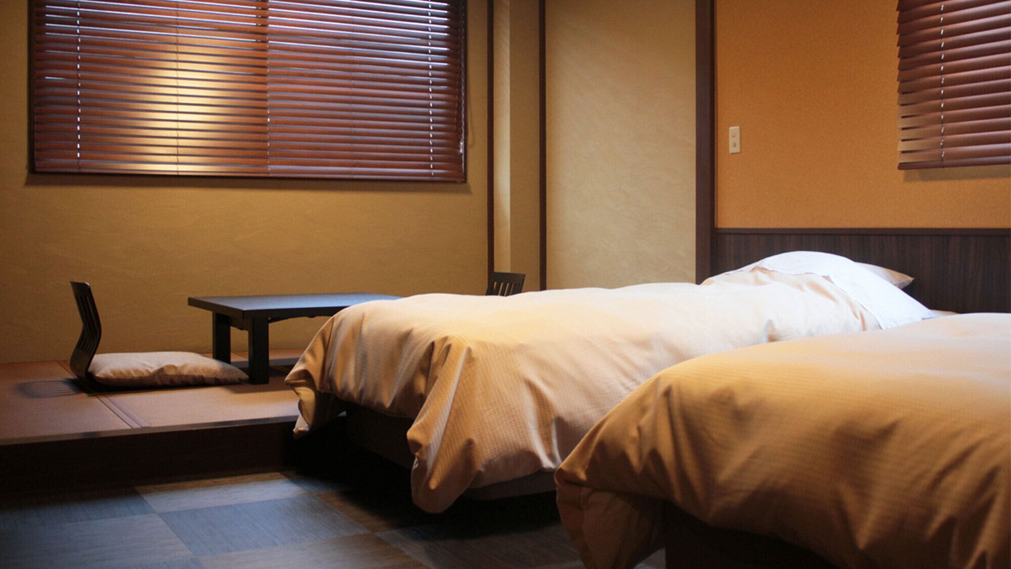 A hotel room with two beds, a small table, and a bench.