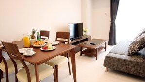 Een hotelkamer met een ontbijt gedekte eettafel, een bank, een televisie en een raam met gordijnen.