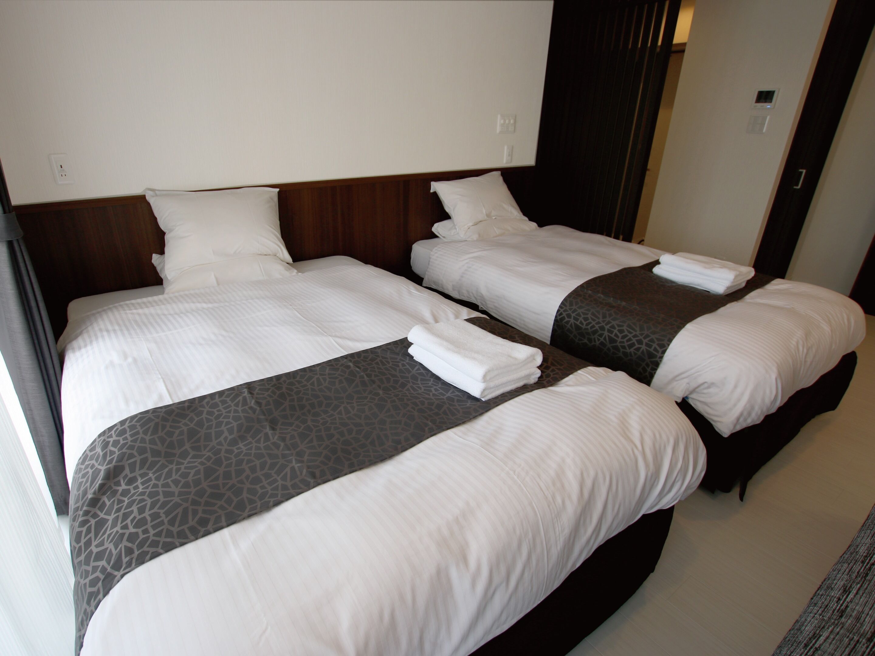 A hotel room with two beds, each with white linens and a grey patterned bedspread.