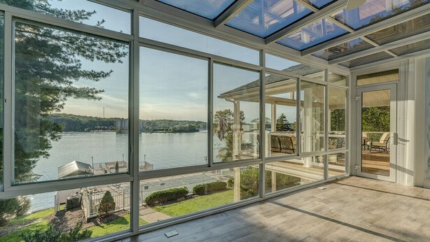 Une pièce spacieuse avec de grandes fenêtres donnant sur un lac, un plafond en verre et une vue sur l’extérieur.