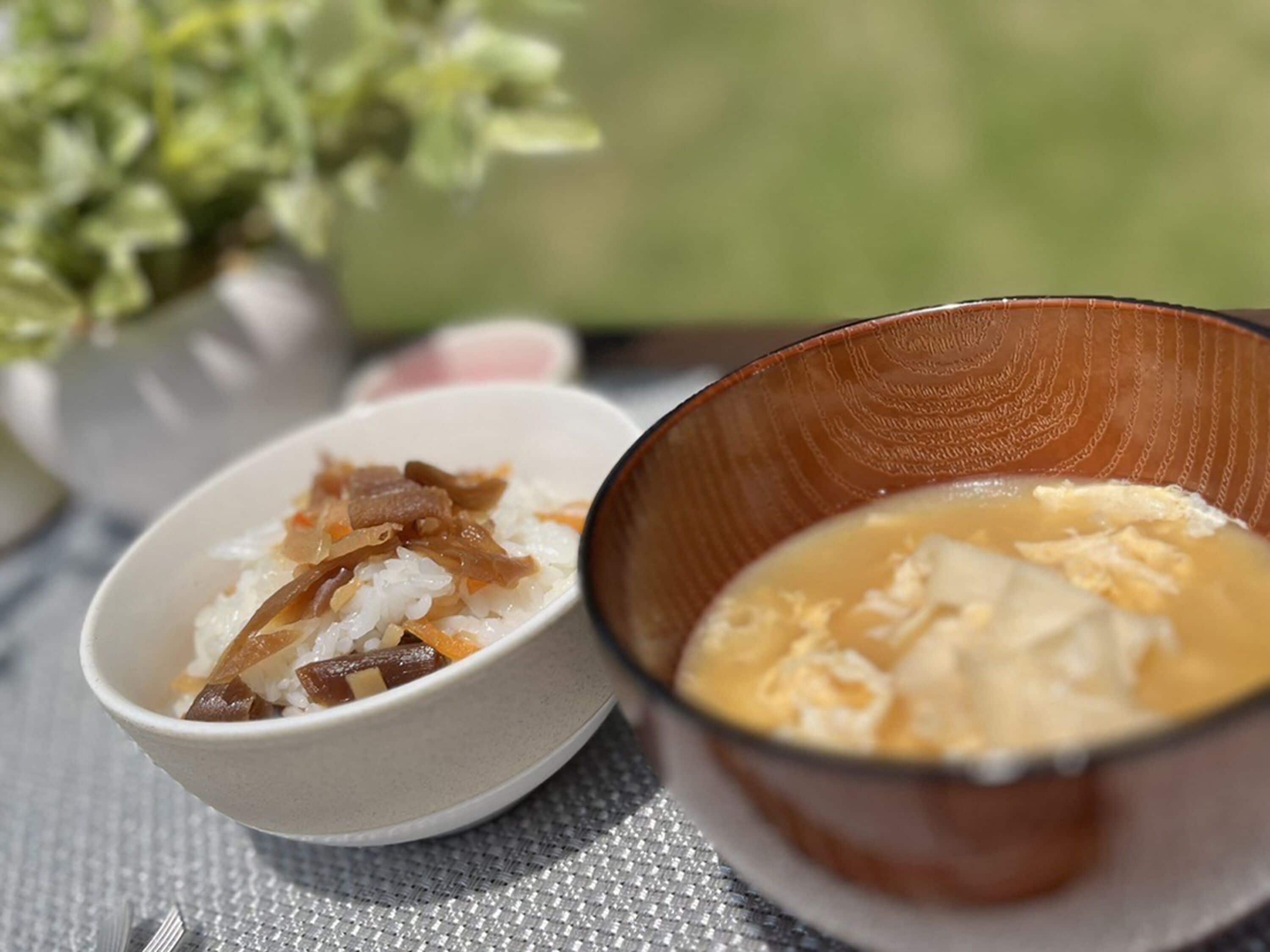 A table with two bowls of food, one containing rice and vegetables, and the other containing a soup.