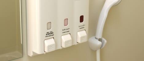 A wall-mounted hotel bathroom with a white hand dryer, a white towel dispenser, and a white hand soap dispenser.