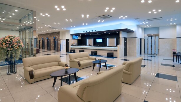 Eine moderne Lobby mit beigen Sofas, einem Empfangstresen und einem großen Spiegel.