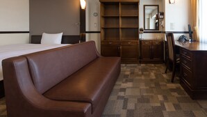 Ein Hotelzimmer mit einem Bett, einem braunen Sofa, einem Schreibtisch mit Telefon, einem Spiegel und einem Kleiderschrank.