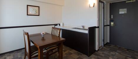 A small kitchenette with a sink, a dining table with chairs, a framed picture on the wall, and a door with a handle.