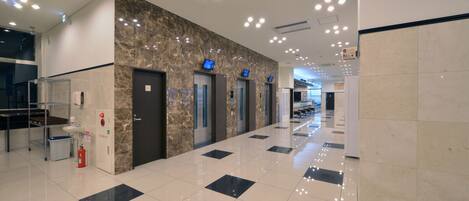 A modern hotel lobby with a marble wall, elevators, and a clean, tiled floor.