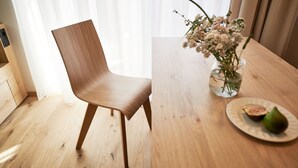 A wooden chair and a table with a vase of flowers and a plate with food. - Apartments Alpe di Susi - Holiday Apartments in the Italian Dolomites (Castelrotto)