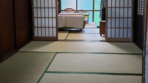 Une pièce de style japonais traditionnel, avec un sol recouvert de tatamis, un lit avec une couvre-lit verte et blanche, et des portes coulissantes en papier de riz (shoji).