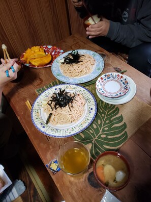 A wooden table with plates of noodles topped with seaweed, a bowl of soup, and a plate of sliced mango. - kominka soratokaze kuuandfuu Ⅱ (Oshima)