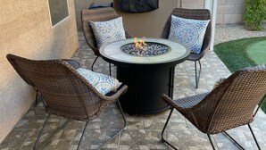 Eine Terrasse mit einem runden Tisch, vier Korbstühlen und einer Feuerstelle.