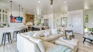 Amplia sala de estar con un sofá seccional beige, una mesa de comedor y una cocina con armarios blancos y electrodomésticos de acero inoxidable.