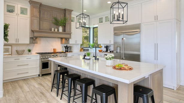 Una cocina moderna con armarios blancos, una isla grande con taburetes de bar, electrodomésticos de acero inoxidable e iluminación colgante.