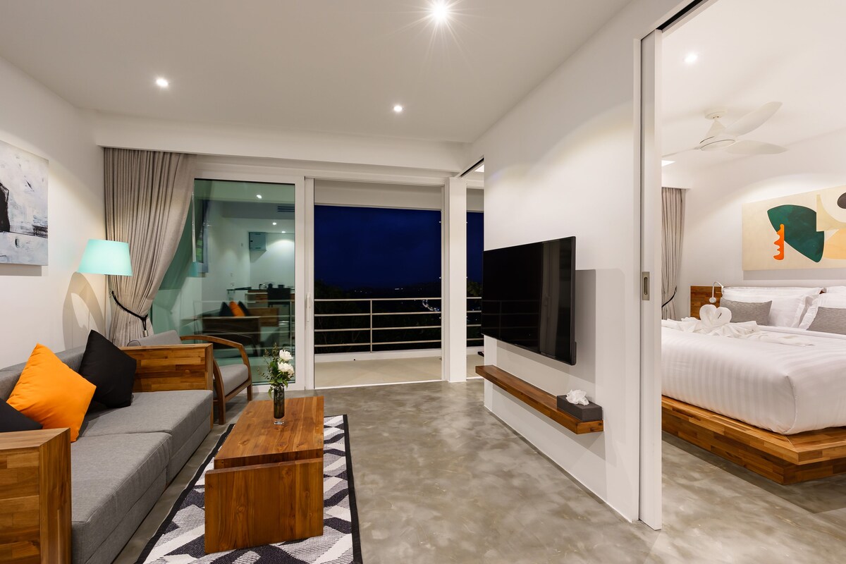 Une chambre d’hôtel moderne équipée d’un canapé, d’une table basse, d’une télévision, d’un lit et d’un balcon avec vue.
