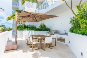 An outdoor patio with a table and chairs, a grill, and a large umbrella.