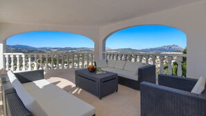 A balcony with wicker furniture, a white sofa, and a coffee table with a fruit bowl. - Large and nice villa  with private pool in Benitachell, on the Costa Blanca, Spain for 8 persons (Benitachell)
